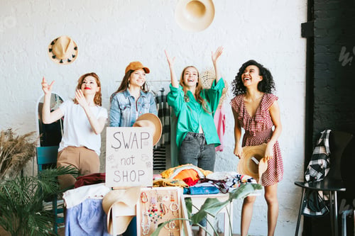 Preview: four young woman female caucasian and african students at swap party try on clothes, bags, shoes and