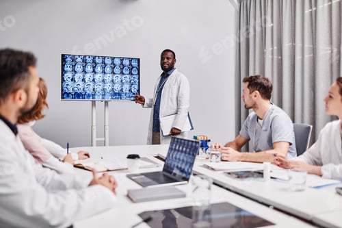Preview: Group of young healthcare workers in lab coats looking at speaker pointing at medical scan of human