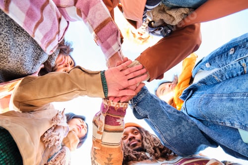 Preview: Low angle view of multiracial group of friends joining hands together.