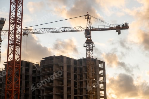 Preview: Cranes are lifting materials at a busy construction site as the sun sets, casting a warm glow over