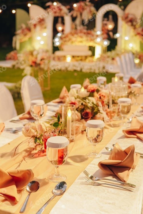 Preview: Night dinner long table with white table cloth and an elegant floral arrangement in the middle.