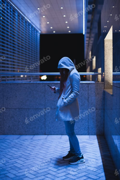 Visualização: Woman using phone texting standing by office building in gray coat, real people using technology