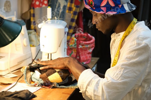 Preview: African tailor sewing a hat with sewing machine at sewing workshop.