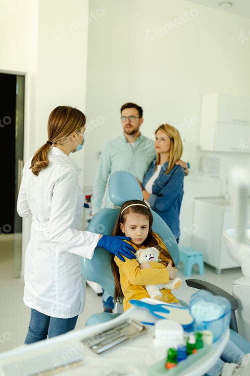 Preview: Worried little girl is sitting in dental chair while doctor discuss with worried parents.