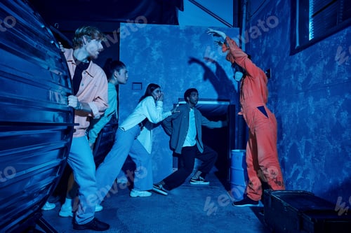 Aperçu: Multicultural group of people escaping from man in gas mask during adventure in quest room