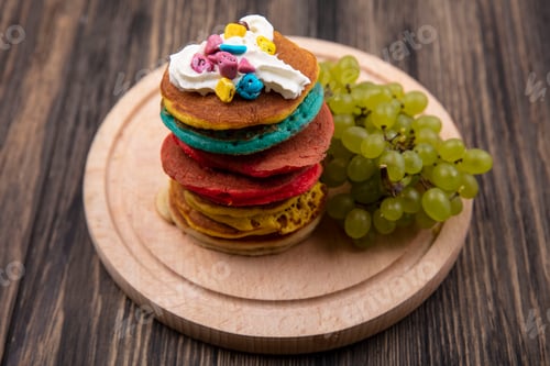 Preview: frontal view multicolored pancakes with cream and green grapes on a stand on a wooden background