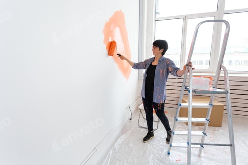 Preview: Renovation, redecoration and repair concept - middle-aged woman painting wall in new home