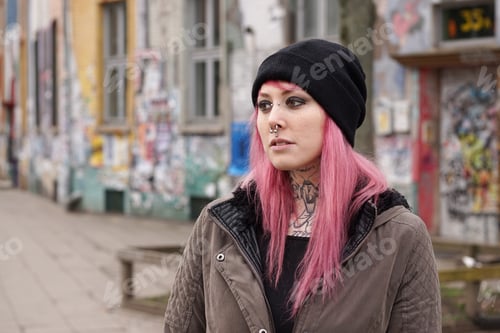 Preview: pierced and tattooed woman in front of graffiti covered building