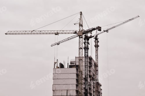 Preview: Working tall cranes inside place for with tall buildings under construction against a clear blue sky