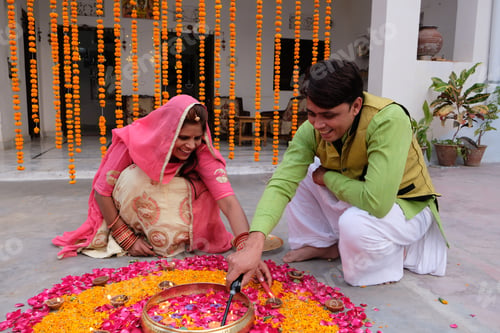 Preview: Indian family creating rangoli on the ground using candles, marigold and pink rose petals