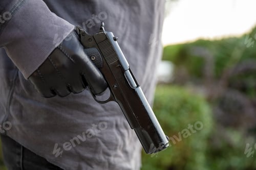 Preview: Gloved hand holding a pistol, blur nature background,