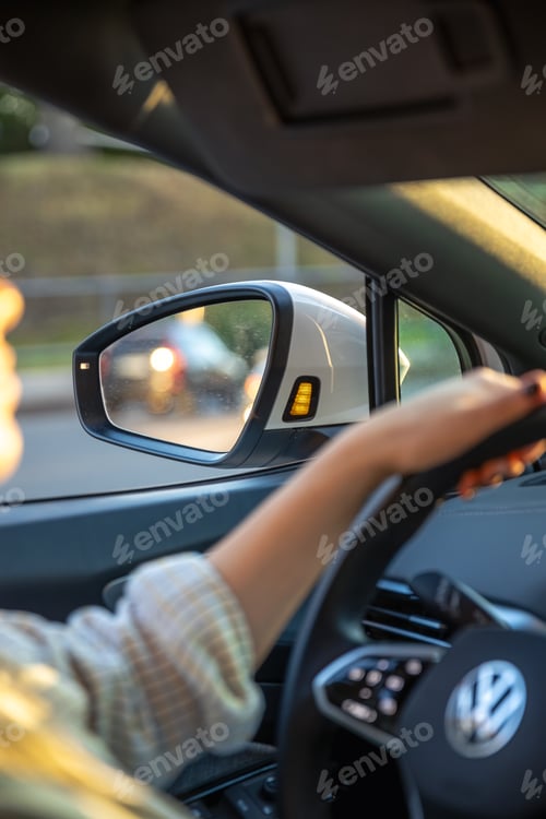 Preview: Young woman driving a car. Hands on the wheel. Side mirror in the car.