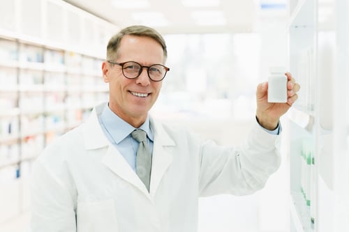Preview: Pharmacist holding jar container of pills remedy looking at camera in drugstore pharmacy