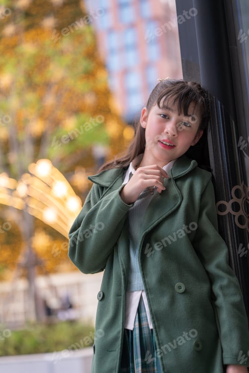 Preview: girl in a green coat decorating a beautifully lit Christmas tree with golden and red ornaments