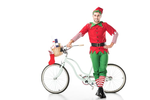 Preview: happy smiling man in christmas elf costume with hand on hip standing near bike with basket full of