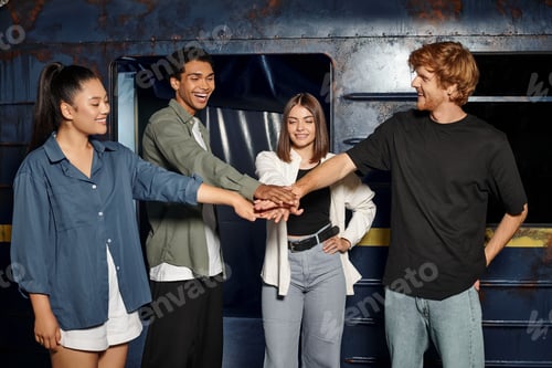 Preview: group of happy multicultural friends staking hands together before quest room game in subway setting