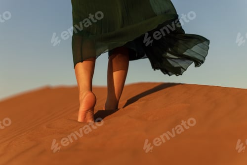 Preview: woman in green long dress stands in desert sand dunes background yellow orange sunset