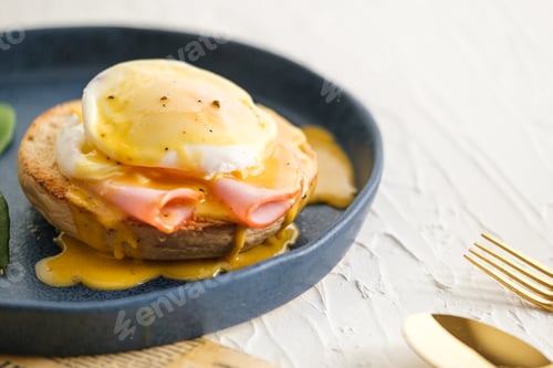 Preview: egg Benedict with hollandaise sauce on blue plate on table in white kitchen