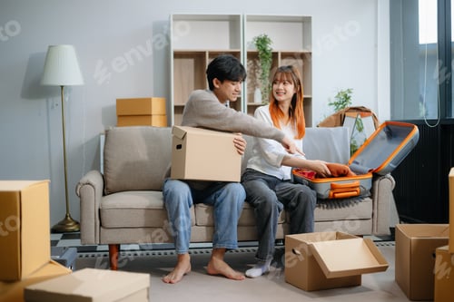 Preview: Young couple preparing for a move, packing boxes and a suitcase in a cozy living room. Perfect for