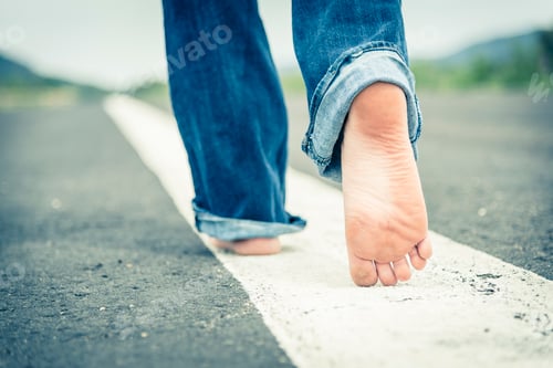 Preview: Young woman walking barefoot on centre line of empty street, partial view