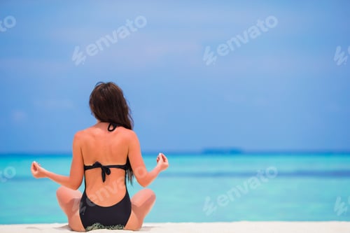 Preview: Healthy young woman sitting in yoga position meditating on the beach