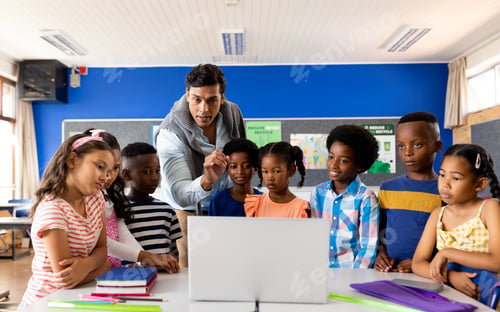 Preview: Biracial male teacher using laptop teaching children in elementary school class