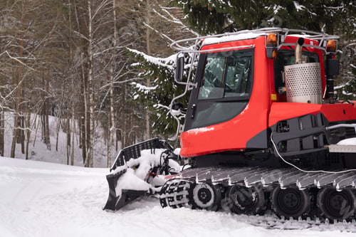 Preview: A snowplow on red tracks standing in winter in the forest near the barn