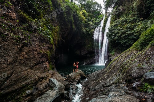 Preview: Lovers at the waterfall, rear view. Couple admiring a beautiful waterfall in Indonesia