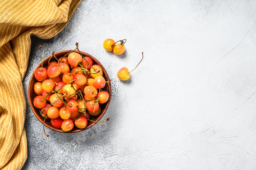 Preview: Mix of yellow and red ripe cherries in a bowl. White background. Top view. Copy space