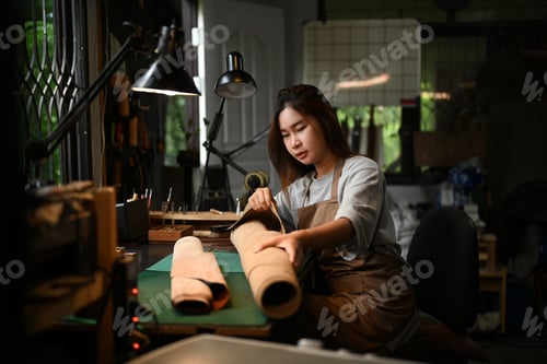 Preview: Portrait of a smiling craftswoman wearing an apron working on leather fabric at her workshop