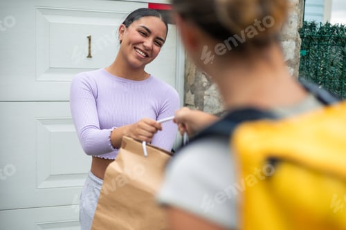 Preview: closeup Food delivery girl seen from behind delivering an order to Latin customer at their doorstep