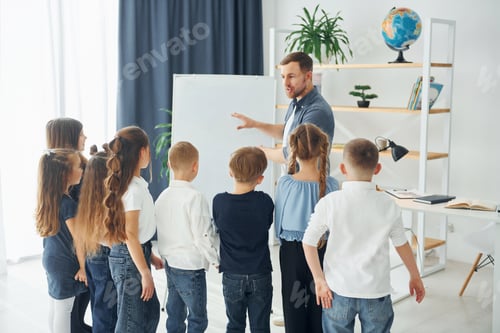 Preview: Explaining lesson and using board. Group of children students in class at school with teacher