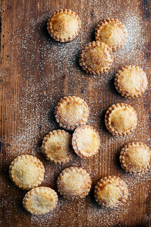 Preview: Freshly baked mince pies, dusted with sugar, on wooden counter, overhead view