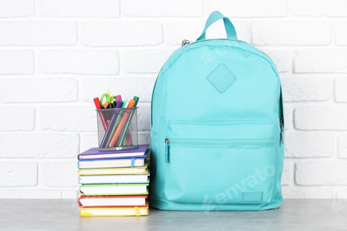 Preview: Backpack with different school stationery on light grey table near brick wall
