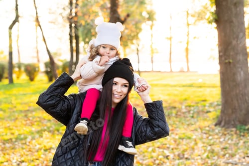 Preview: Mother and young little girl are playing in an autumn park on a yellow and orange leaf background