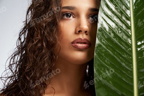 Visualização: Young woman hiding face behind big green leaf