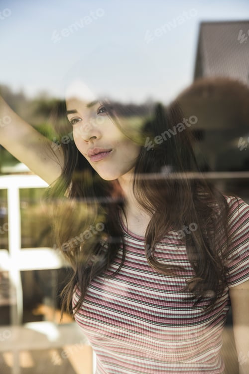 Preview: Portrait of pensive young woman behind windowpane