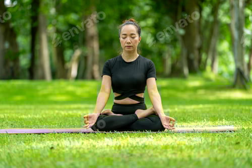 Preview: A woman is sitting on a mat in a park, practicing yoga