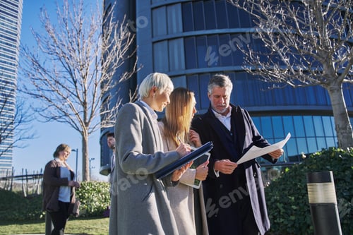 Preview: Three businessmen outside office building with documents discussing plans,