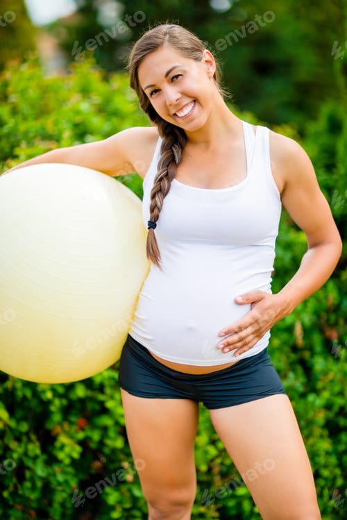 Preview: Happy Pregnant Woman Touching Abdomen While Holding Fitness Ball