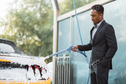 Preview: Portrait of handsome bearded young African businessman washing his yellow car with foam