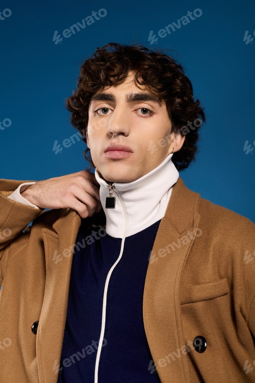 Preview: Young stylish man showcases modern fashion with confidence against bright blue backdrop