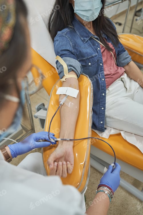 Preview: Female patient in mask donating blood in modern clinic
