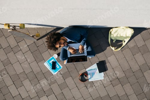 Preview: Young businessman sitting outdoors at a wall working on laptop