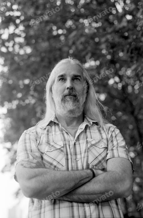 Preview: Thoughtful farmer looking up with crossed arms in monochrome analog film