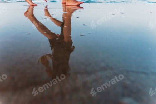Preview: Two friends walking at sunset on a beach, reflecting in the puddles of sand.