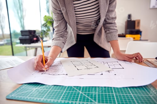Preview: Close Up Of Female Architect Standing Working In Office Studying Plans For New Building