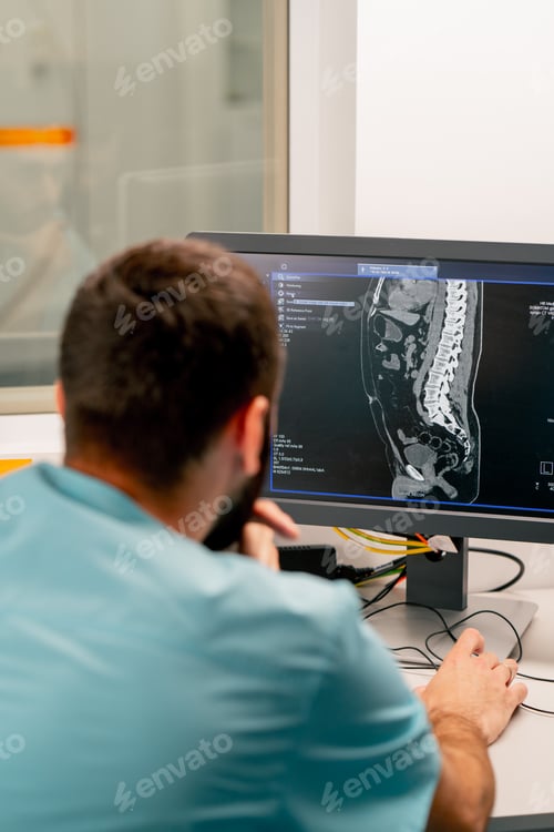 Preview: A radiologist sits at a table behind a computer monitor and examines a magnetic resonance imaging