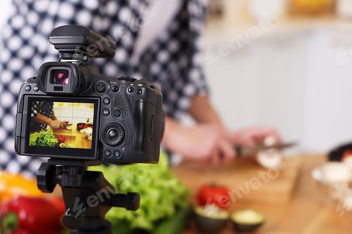 Preview: Food blogger cooking while recording video in kitchen, focus on camera