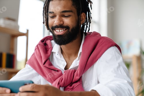 Preview: Joyful african american guy smiling and playing video game on cellphone